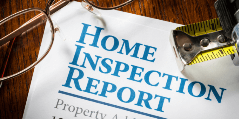A printed home inspection report with glasses and a tape measurer.